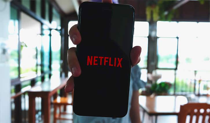 An image featuring Netflix concept with a person holding their phone that has Netflix opened